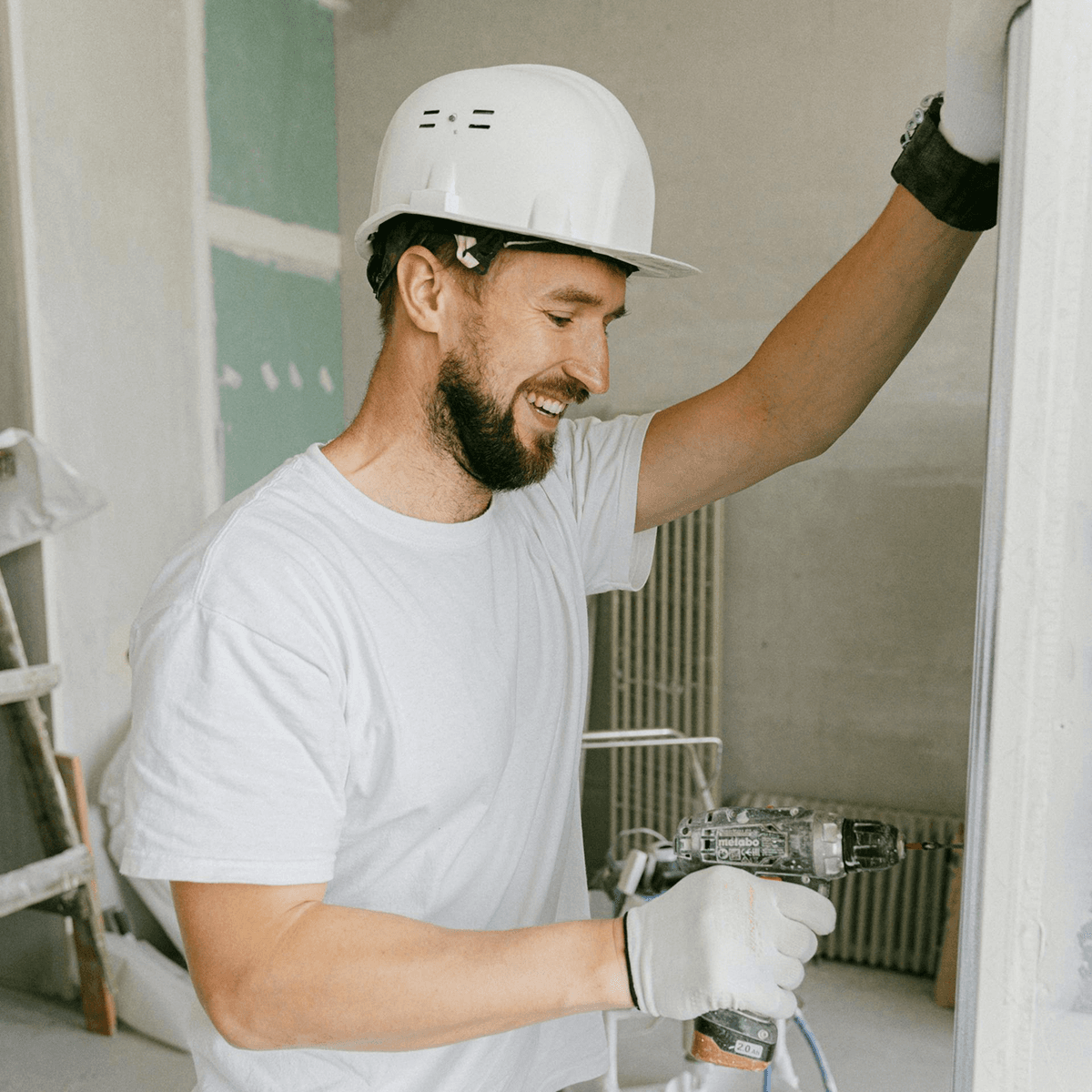 Smiling contractor in a hard hat using a power drill during construction work